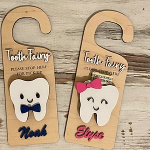 May include: Two wooden tooth fairy doors with a tooth cutout and a space for a lost tooth. The door on the left is blue and says "Noah" and the door on the right is pink and says "Elyse".