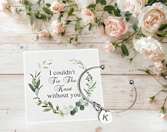 May include: A white card with green foliage and the text "I couldn't Tie The Knot without you". A silver bangle bracelet with a knotted charm and a letter K charm is on top of the card.