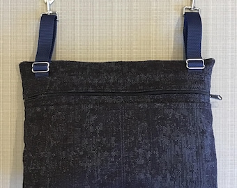 May include: A black zippered pouch with two adjustable straps and silver clasps. The pouch has a textured fabric design.