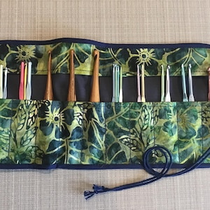 May include: A green and blue floral fabric roll-up case with a navy blue trim and a navy blue drawstring closure. The case is filled with a variety of crochet hooks.