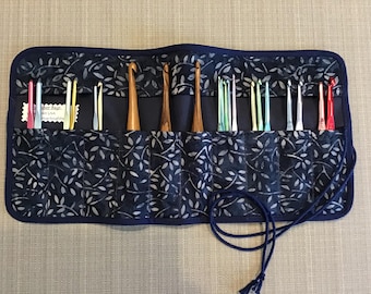 Puede incluir: Un rollo de tela azul con un patrón de hojas blancas, que contiene una variedad de agujas de crochet. El rollo tiene un cierre de cordón y una etiqueta que dice "Fisher Rags, NY USA".