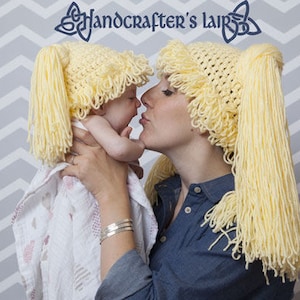 May include: A woman and a child wearing yellow crocheted hats with long yarn tails. The hats are styled like pigtails. The woman is holding the child in her arms and they are looking at each other.