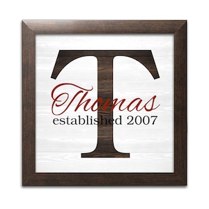 May include: A framed wood sign with a white background and a large black letter "T" with a wood grain texture. The text "Thomas established 2007" is written in red cursive below the letter.