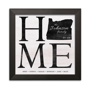 May include: Black and white framed print with the word "HOME" in large letters. The state of Oregon is outlined in black with the text "the Johnson family EST. 2008". Below the word "HOME" are the names "MIKE, CHERYL, SARAH, MORGAN, JAKE, SEAN".