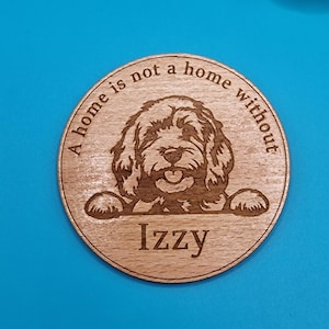 May include: A round wooden coaster with a laser-engraved image of a dog with the text "A home is not a home without" and the name "Izzy" underneath the dog.
