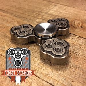 Può includere: Uno spinner fidget in metallo argentato con un design a trifoglio. Lo spinner ha tre bracci e un cuscinetto centrale. Il cuscinetto è in acciaio inossidabile.