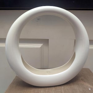 以下が含まれることがあります： 滑らかで光沢のある仕上げの、大きくて白い円形のセラミック花瓶。 花瓶はユニークなオープンデザインで、幅広で丸みを帯びた形状をしています。 内側は明るい白の色合いです。 花瓶は装飾的な家のアクセントです。