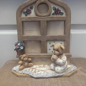 Könnte beinhalten: Ein dekorativer Bilderrahmen mit Fensterdesign, der zwei Öffnungen für Fotos aufweist. Der Rahmen ist mit floralen Akzenten verziert und enthält zwei Teddybär-Figuren. Der Text "God Bless..." ist sichtbar.