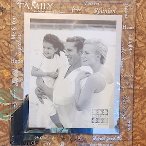 Könnte beinhalten: Ein Bilderrahmen aus Glas mit einem Schwarzweißfoto einer dreiköpfigen Familie. Der Rahmen hat einen dekorativen Rand mit den Worten "Family", "Forever Reunion", "Dreams", "Home", "Laughter", "All Heart", "Comfort and Warmth", "Heritage", "Enjoy", "Love", "Memories", "Happy", "Together", "Share good times", "Cherish Good Memories".