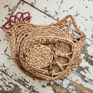 May include: A woven wicker chicken-shaped trivet with a red and white comb. The trivet is made from natural materials and has a rustic, farmhouse style.