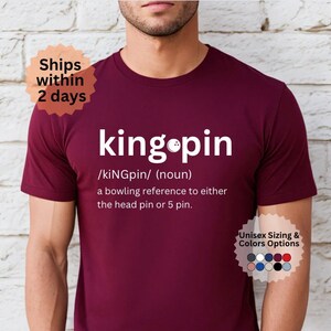 May include: Burgundy t-shirt with a white graphic that says "king pin" and defines the word as a bowling reference to either the head pin or 5 pin.