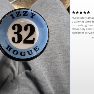 Pode incluir: Um taco de beisebol azul e branco com o nome "IZZY" e o n&uacute;mero "32" nele. O taco tamb&eacute;m tem a palavra "HOGUE" escrita nele. O taco est&aacute; sentado em uma superf&iacute;cie cinza. "Qualidade absolutamente incr&iacute;vel! Parece linda no taco da minha filha. E um servi&ccedil;o ao cliente absolutamente incr&iacute;vel!" - Cliente Etsy