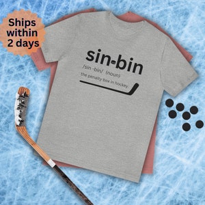May include: A gray t-shirt with the text "sin-bin" defined as "the penalty box in hockey."  The text is in black with a black hockey stick graphic.