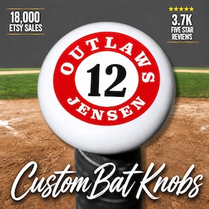 Puede incluir: Un pomo de bate de béisbol blanco y redondo con un borde circular rojo que presenta el texto negro OUTLAWS y JENSEN rodeando el número 12 en el centro. El pomo está unido a un mango de bate cilíndrico negro sobre un campo de béisbol.