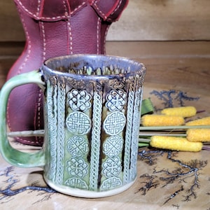 May include: A set of three ceramic mugs with a speckled, matte finish. The mugs are in shades of cream, light gray, and dark gray. Each mug has a simple, modern design and a rounded handle.