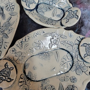 May include: A set of three ceramic serving dishes with a light beige background and a blue floral design. The dishes feature a repeating pattern of hibiscus flowers, leaves, and sea turtles.