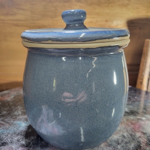 May include: A blue ceramic jar with a lid. The jar has a speckled glaze and a white rim around the top. The lid is also blue and has a knob on top.