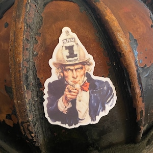 May include: A vintage-style Uncle Sam sticker with a red, white, and blue color scheme. He is wearing a blue jacket, a white shirt, and a red bow tie. He is pointing with his right hand and has a serious expression on his face. The sticker has the text "I WANT YOU" and "SAM" on it.