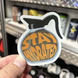 May include: A white sticker with a cartoon image of a coffee pot with the text "Stay Hydrated" in orange letters.