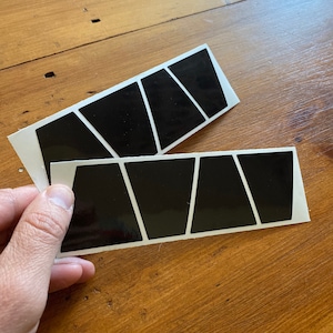 May include: Two sheets of black vinyl stickers with a geometric design. Each sheet has six black triangles arranged in a staggered pattern.