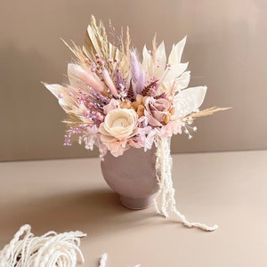 Peut inclure: Un arrangement de fleurs séchées dans un vase en céramique gris clair. L'arrangement comprend des fleurs séchées dans des tons de rose, beige et blanc, notamment de l'herbe de la pampa, des queues de lapin et des roses.