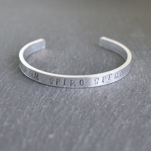 Puede incluir: Un brazalete de plata con la inscripción "Dum Spiro Spero" grabada en la banda.
