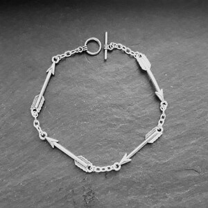 Può includere: Un braccialetto d'argento con una catena e ciondoli a forma di freccia. Il braccialetto ha una chiusura a scorrimento.