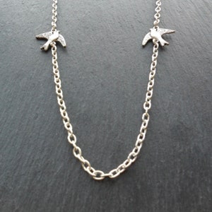 May include: A silver chain necklace with two small silver bird charms.