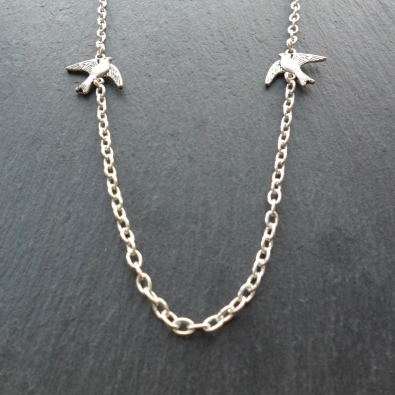 May include: A silver chain necklace with two small silver bird charms.
