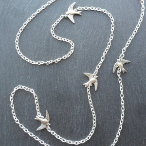 May include: A silver chain necklace with four silver bird charms. The necklace is on a gray background.