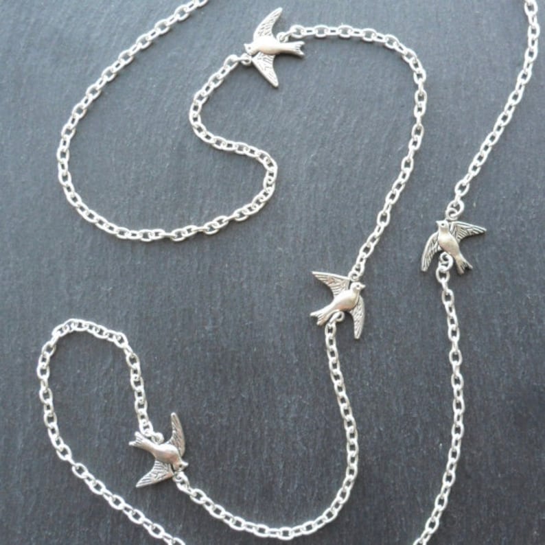 May include: A silver chain necklace with four silver bird charms. The necklace is on a gray background.