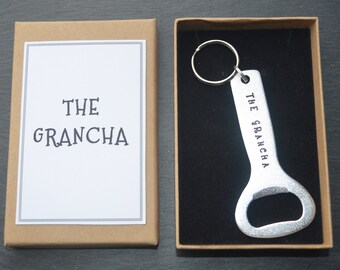 May include: A silver bottle opener with a keychain ring. The bottle opener has the text "THE GRANCHA" engraved on it. The bottle opener is in a brown box with a white label that says "THE GRANCHA".