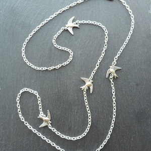 May include: A silver chain necklace with five silver bird charms. The chain is long and has a delicate design. The birds are facing different directions and are in flight.