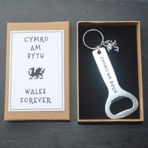May include: A silver bottle opener with a dragon charm and a key ring. The bottle opener is engraved with the text "CYMRU AM BYTH" and "WALES FOREVER".