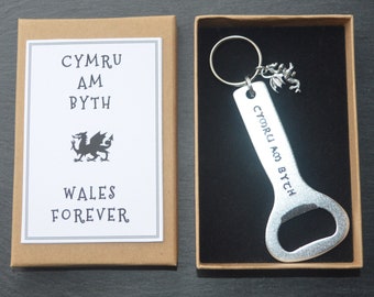 May include: A silver bottle opener with a dragon charm and a key ring. The bottle opener is engraved with the text "CYMRU AM BYTH" and "WALES FOREVER".
