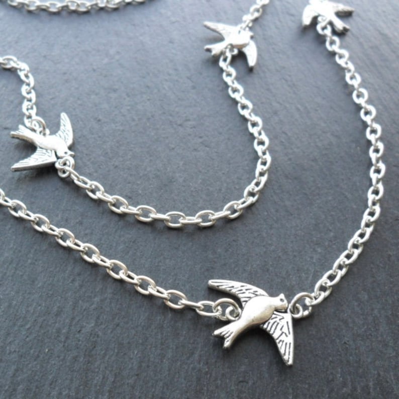 May include: Silver chain necklace with multiple silver bird charms. The necklace is layered and has a delicate chain.