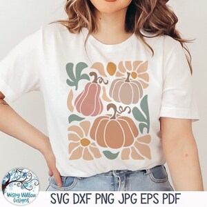 May include: A white t-shirt with a design of stylized pumpkins and flowers in shades of pink, orange, and green. The design is in a geometric style.