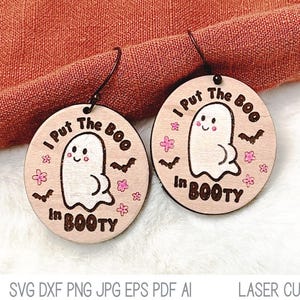 May include: A pair of wooden earrings with a ghost design. The earrings are painted with pink flowers and bats. The text on the earrings reads "I Put The Boo In Booty".