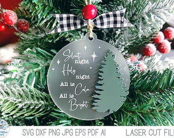 May include: A circular frosted acrylic Christmas ornament featuring the white text Silent night Holy night All is Calm All is Bright and a green pine tree silhouette. It is topped with a black and white buffalo plaid ribbon and a red bead.