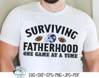 以下が含まれることがあります： 「SURVIVING FATHERHOOD」という黒い文字が、青いフットボールヘルメットと2つの茶色のフットボールのイラストの上に配置され、その下に「ONE GAME AT A TIME」という黒い文字がプリントされた白い半袖Tシャツ。