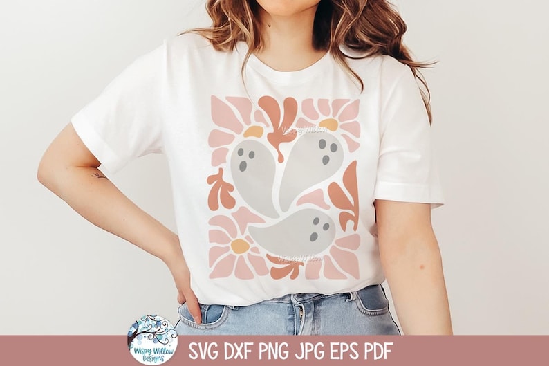 May include: A white short-sleeve t-shirt featuring a central graphic print of three light gray ghosts surrounded by stylized pink flowers and abstract orange shapes. The design is arranged in a square pattern on the front of the garment.