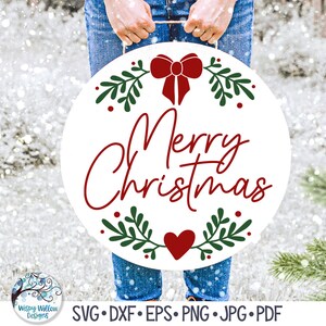 May include: A white round sign with a red bow, green leaves, and red berries. The sign says "Merry Christmas" in red cursive lettering. A red heart is at the bottom of the sign.