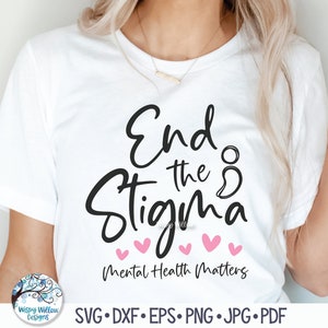May include: A white short-sleeved t-shirt featuring black cursive text that reads End the Stigma with a semicolon symbol, five small pink hearts underneath, and the additional black text Mental Health Matters printed at the bottom of the design.
