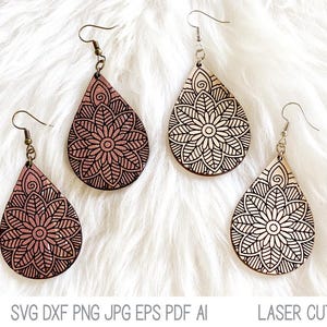 May include: Two pairs of teardrop-shaped earrings featuring intricate black mandala patterns. One pair is a light wood tone, and the other is a mauve-pink wood tone. Each earring hangs from a silver-toned metal hook. Text at the bottom reads: SVG DXF PNG JPG EPS PDF AI LASER CUT FILE.