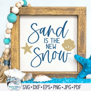 May include: A wooden sign with the text "Sand is the new snow" in blue cursive lettering. A gold star and seashell are on the sign. The sign is sitting on a blue surface with seashells and a blue starfish.