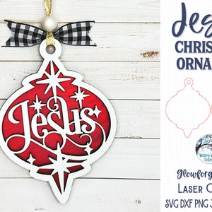 May include: A decorative Christmas ornament featuring a red background with white star accents and the word Jesus in white script. The ornament is topped with a black and white buffalo plaid ribbon and a white bead, hanging from a gold string.
