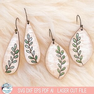 May include: Two pairs of wooden earrings with a light wood grain finish, featuring a hand-drawn green leaf vine design. The earrings include two elongated teardrop shapes and two wider leaf shapes, all equipped with dark metal hook ear wires.