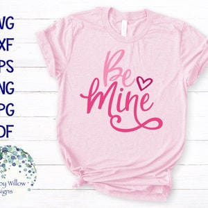 May include: Pink t-shirt with the text "Be Mine" in a pink and red gradient font with a small pink heart.