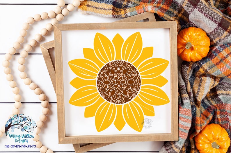 K&ouml;nnte beinhalten: Ein quadratischer Holzrahmen mit einem wei&szlig;en Schild, das eine gro&szlig;e gelbe Sonnenblumenillustration zeigt. Die Sonnenblume hat eine detaillierte braune Mitte im Mandala-Stil mit komplexen wei&szlig;en Linienmustern. Die Bl&uuml;tenbl&auml;tter sind einfarbig gelb.
