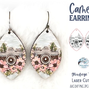 May include: Wooden teardrop earrings featuring a camera design with pink flowers and green leaves. The earrings have a light blue background and the text "Camera EARRINGS". The earrings are laser cut.